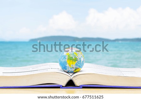 The globe rests on a book that turns out, the backdrop is sky and mountains sea.