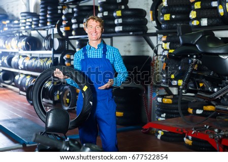Mature friendly mechanic holding new tyre for motorcycle in workshop