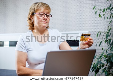 Old people and modern technology concept. Portrait of a 50s mature woman hand holding credit card, using online internet payment at home. Indoor senior people living lifestyle.