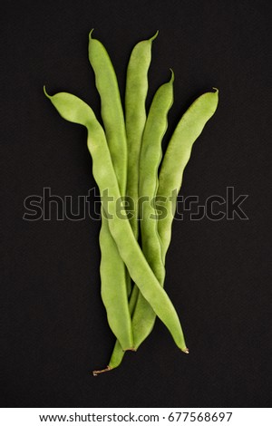 String of young beans on a black textured background.
