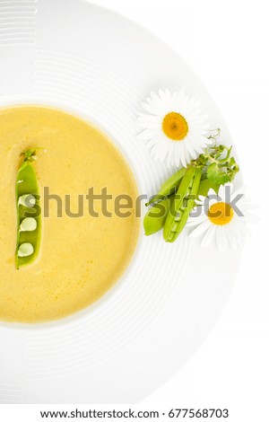 Pea Sticks and Flowers Daisies on the edge of a white plate with a pea soup cream on a white background.