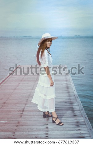 Young beautiful woman standing on wooden bridge on a background of the sea.
