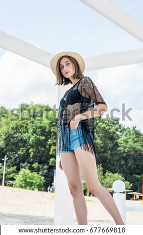 Beautiful slim young girl in a straw hat standing on a white lounger on the beach