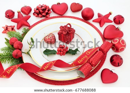 Christmas dinner place setting with porcelain plates, holly, mistletoe and fir, red bauble decorations and decorative ribbon on white background