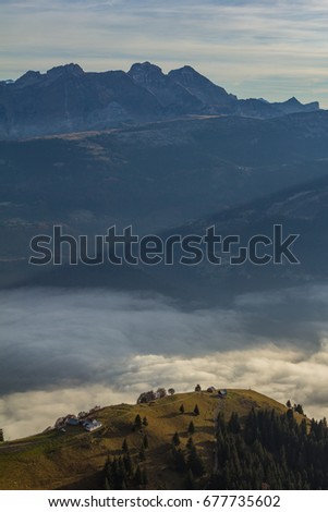 Mountain hill with country houses with trees over the sea of fog with mountains in background