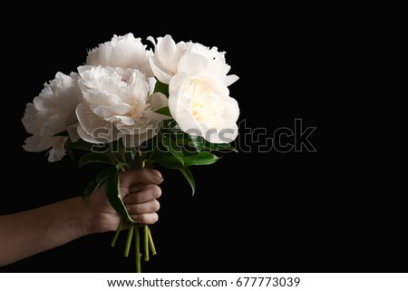 Female hand with bouquet of peony flowers on dark background