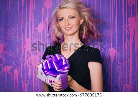 Birthday. A beautiful girl with white hair and black clothes is holding a gift in her hands. Model with purple hair strands on a bright background. The surprise