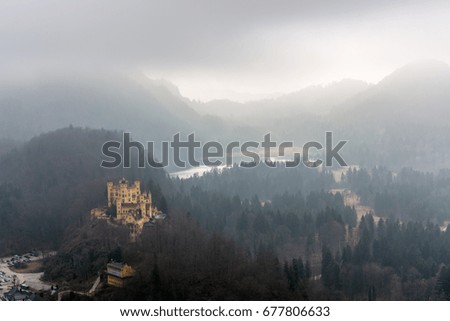 The castle Hohenschwangau and the lake Alpsee on a foggy day with some sun rays coming through