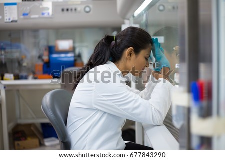 Closeup portrait, tired young woman scientist,crashing, with failed experiments and working long hours, leaning head against glass fume hood with mirror reflection. Isolated laboratory Royalty-Free Stock Photo #677843290