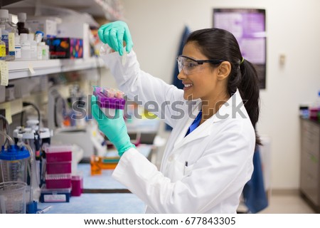 Closeup portrait, young scientist in labcoat wearing nitrile gloves, doing experiments in lab, academic sector. Royalty-Free Stock Photo #677843305