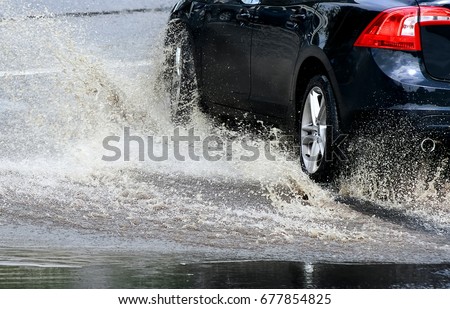 Car splashes through a large puddle on a flooded street. Motion car, rain, big puddle of water spray from the wheels