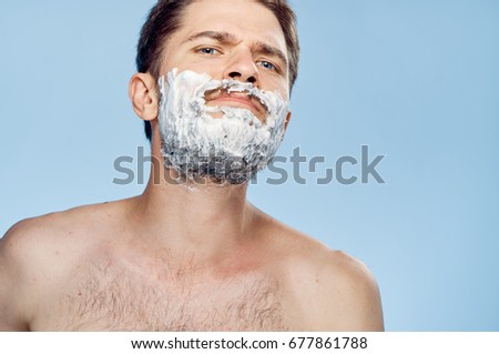 Young guy with a beard on a blue background in shaving foam.