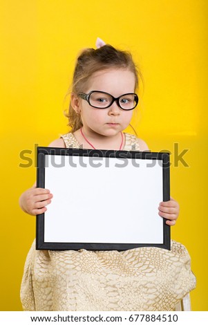 Little girl with board in beautiful dress and glasses on yellow background