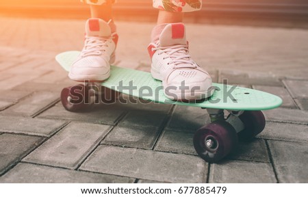 Young skater girl in pink slip on shoes ride colorful tiny skateboard deck outdoors in summer.Sunlight and warm weathe are great for skateboarding in the city,outdoor skate park.Popular sport activity