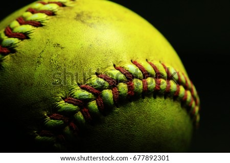 Yellow softball closeup with red seams on black background.