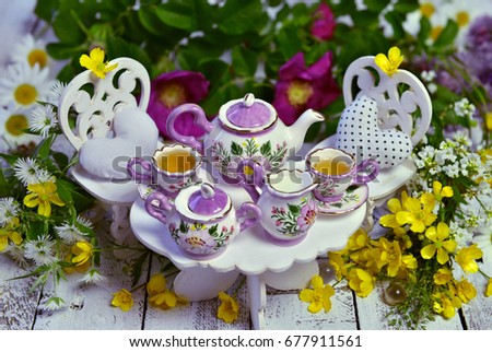 Mad tea party concept with decorated small furniture, cups, teapot and flowers on planks. Alice in Wonderland background, fairy tale abstract concept. Still life of mad tea party