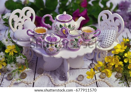 Mad tea party concept with small table, chairs, cups and teapot and with wild flowers. Alice in Wonderland background, fairy tale abstract concept. Still life of mad tea party