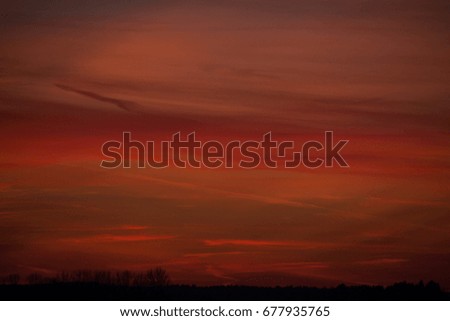 Colorful evening sky with red cloudscape and stripes illuminated by the sun after sunset