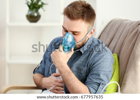 Young man using nebulizer for asthma and respiratory diseases at home Royalty-Free Stock Photo #677957635