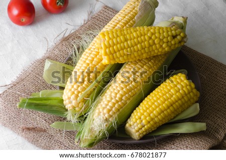 Fresh tomatoes, boiled and raw corn with leaves in a plate on a sackcloth in rustic style. Top view Royalty-Free Stock Photo #678021877