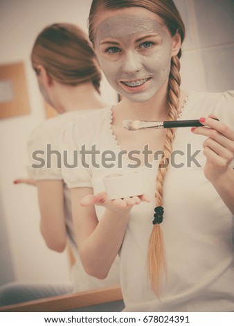 Skincare. Blonde woman in bathroom applying with brush gray clay mud mask to her face. Young lady taking care of skin. Spa beauty wellness.