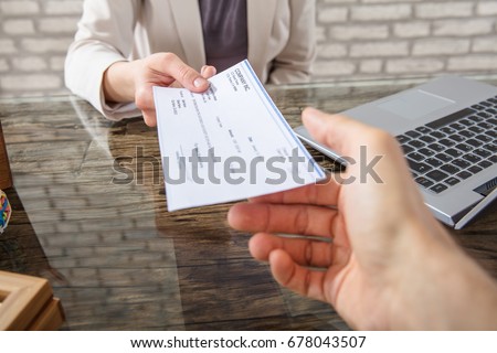 Close-up Of A Business Woman Giving Cheque To Her Colleague At Workplace In Office Royalty-Free Stock Photo #678043507