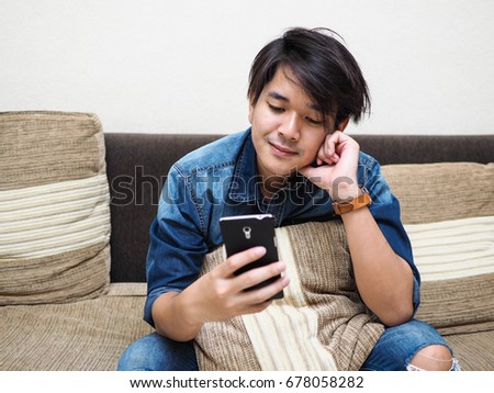 young Asian man smiling and happy when look at smartphone on sofa at home office.a man use smartphone for device on internet technology.