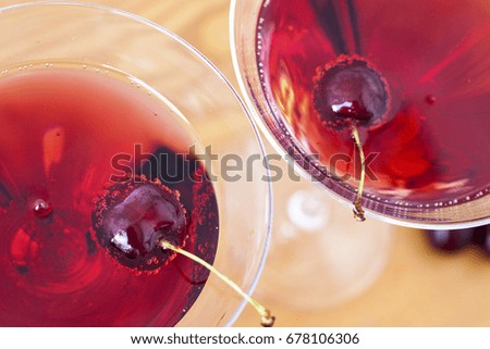 Cold alcoholic cocktail with cherry on the sunny table background. Top view, macro.