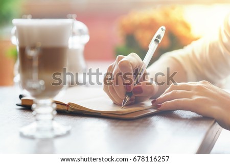 woman's hand with red nails writing some message note or letter to notebook by pen at sunny day