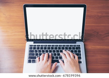 Mockup image of hand using and typing on laptop with blank white screen on wooden table in office