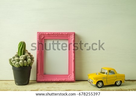 Vintage pink photo frame on old wooden table with cactus and car over white wooden background