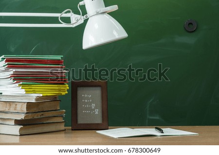 Teacher or student desk table. Education background. Education concept. Stacked books, copybook, handbook, photo frame and lamp on the table.