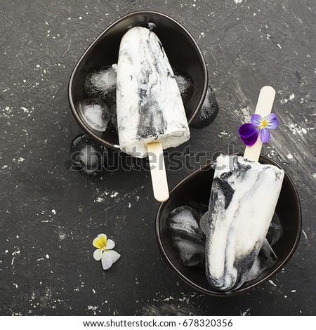 Yoghurt refreshing marble ice cream popsicle in trendy fashion colors on a dark background with edible flowers of garden violas. Selective focus. Top View.