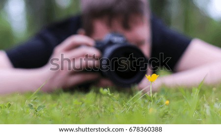 A man photographing a flower growing on grass.