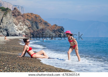 mother and her little daughter in the red swimsuit on the beach