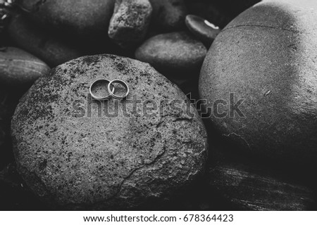 Wedding golden silver engagement rings on the background of a round big stones. Close up. Black and white photo. Place for text.