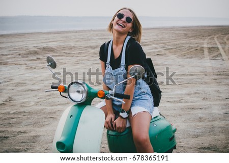 Young female laughing while sitting on retro scooter on the beach