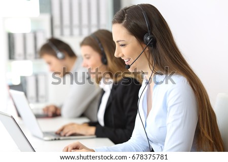 Side view of a telemarketer working on line at office with other workers in the background Royalty-Free Stock Photo #678375781