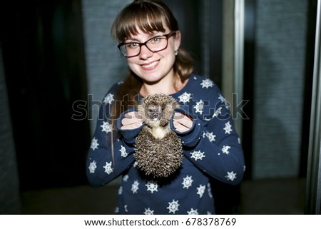 The girl is holding a hedgehog on her hands. The hedgehog licking milk