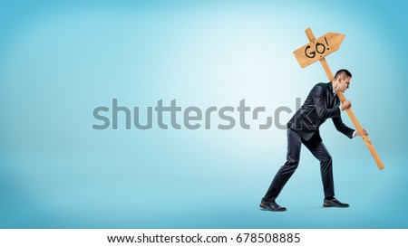 A businessman on blue background holding a heavy road sign with a 'Go' writing on it. Hard work. Right motivation. Road to success.