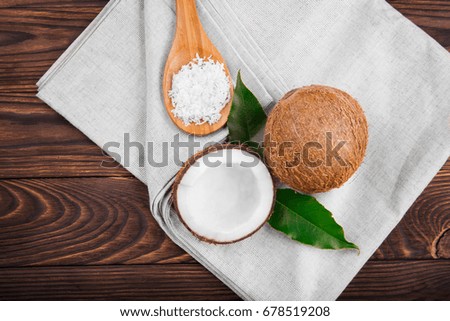 Nutritious exotic whole and cut nuts with green leaves and a wooden spoon full of coconut chips on a grey fabric and on a dark brown wooden background. Fresh coconut products.