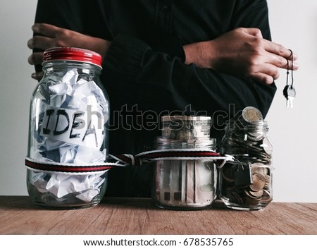 Business savings idea, Businessman use calculator and pen, Jar with crumpled paper "IDEA" word tie  with jar full of money currency and coins bind together chain lock key and scissors  on wood table