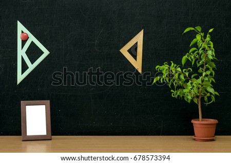 Teacher or student desk table. Education background. Education concept. Green plant tree and photo frame on blackboard background.