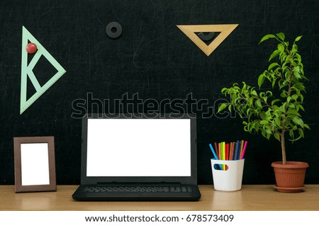 Teacher or student desk table. Education background. Education concept. Laptop with blank screen, green plant tree, book (copybook), colour pencils, photo frame on blackboard.