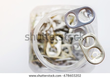 Selective focus picture of Silver bronze and Golden bronze color aluminum pull tabs on top of plastic box, recycle idea