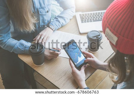 Cose-up smartphone with graphs and charts, diagrams on screen in female's hands. Meeting of two businesswomen in cafe.Girls working, learning online.First woman takes notes, second uses smartphone Royalty-Free Stock Photo #678606763