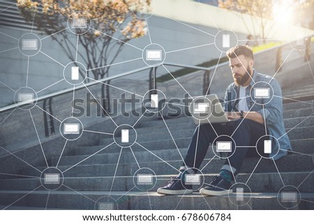 Young businessman sits outdoor on steps, using laptop.Blockchain technology. Trading on stock exchange. Hipster bearded man is working, learning online.Education for adults.Social network.Film effect