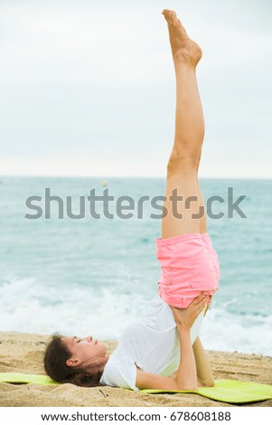 Smiling adult woman in white T-shirt is doing excercises on endurance on the beach.