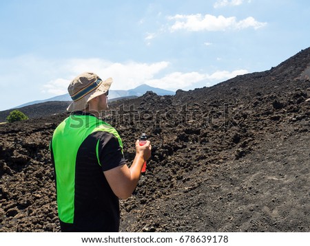 young man hiker looks the Etna's Valley While the volcano smokes. picture take from the back side while the guy holding and drinking an energy beverage