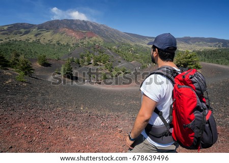 young man hiker looks the Etna's Valley While the volcano smokes. picture take from the back side while the guy dress his backpack